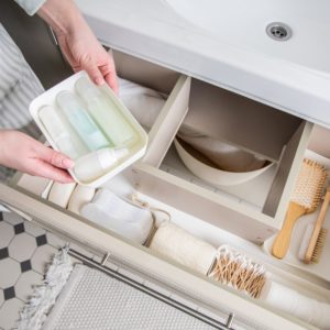 Housewife hands putting rolled up towel into open drawer under sink. Female organizing storage space in bathroom top view. Woman cleaning housework at home. Modern Marie Kondo's keeping method